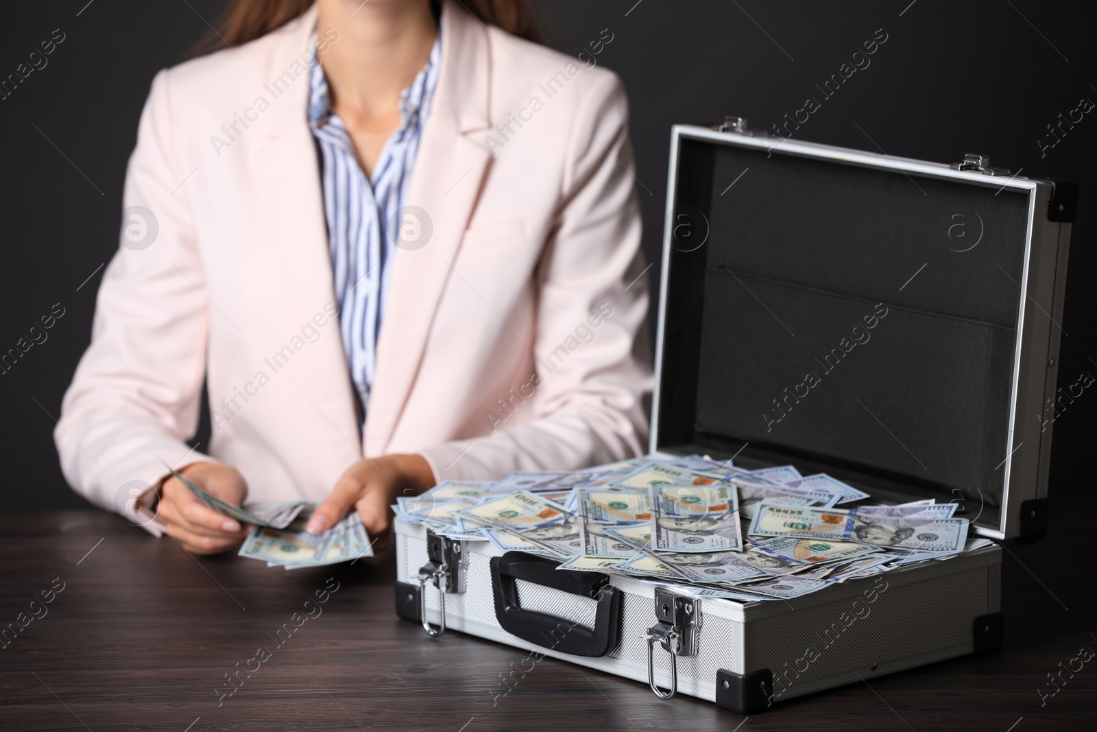 Photo of Businesswoman with case of dollar bills at wooden table, closeup