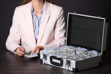 Photo of Businesswoman with case of dollar bills at wooden table, closeup