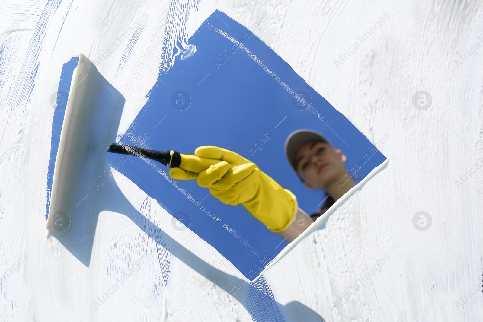 Photo of Woman cleaning glass with squeegee on sunny day