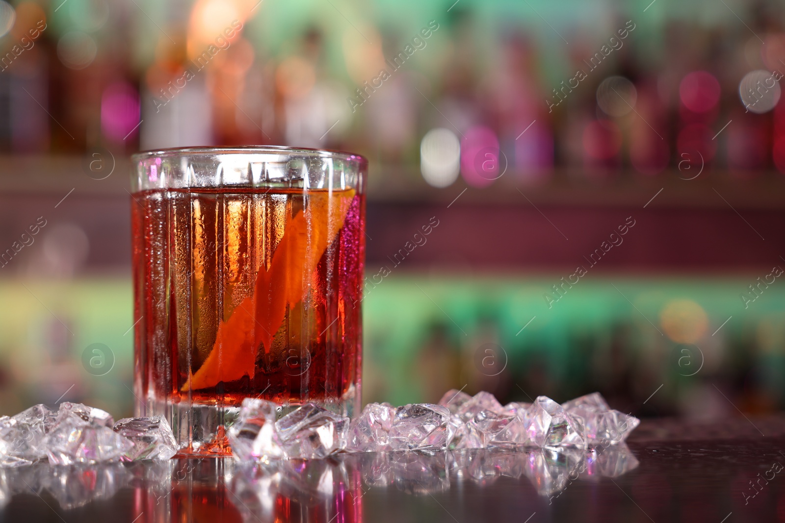 Photo of Fresh alcoholic Negroni cocktail and ice cubes on counter in bar, closeup. Space for text