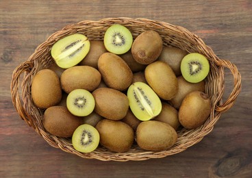 Photo of Basket of many whole and cut fresh kiwis on wooden table, top view