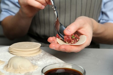 Photo of Woman putting gyoza filling in center of dough wrapper at light grey table, closeup