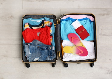 Photo of Packed suitcase with summer clothes and passport on wooden background, top view