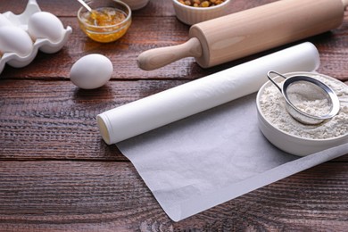 Roll of baking parchment paper and ingredients on wooden table