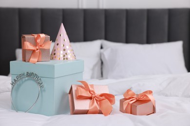 Photo of Many gift boxes, headband and party hat on bed in room. Happy Birthday