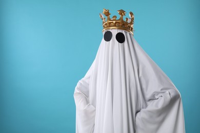 Person in ghost costume and luxurious crown on light blue background, space for text