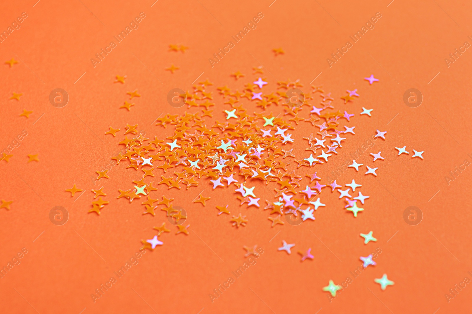 Photo of Shiny bright glitter on orange background, closeup