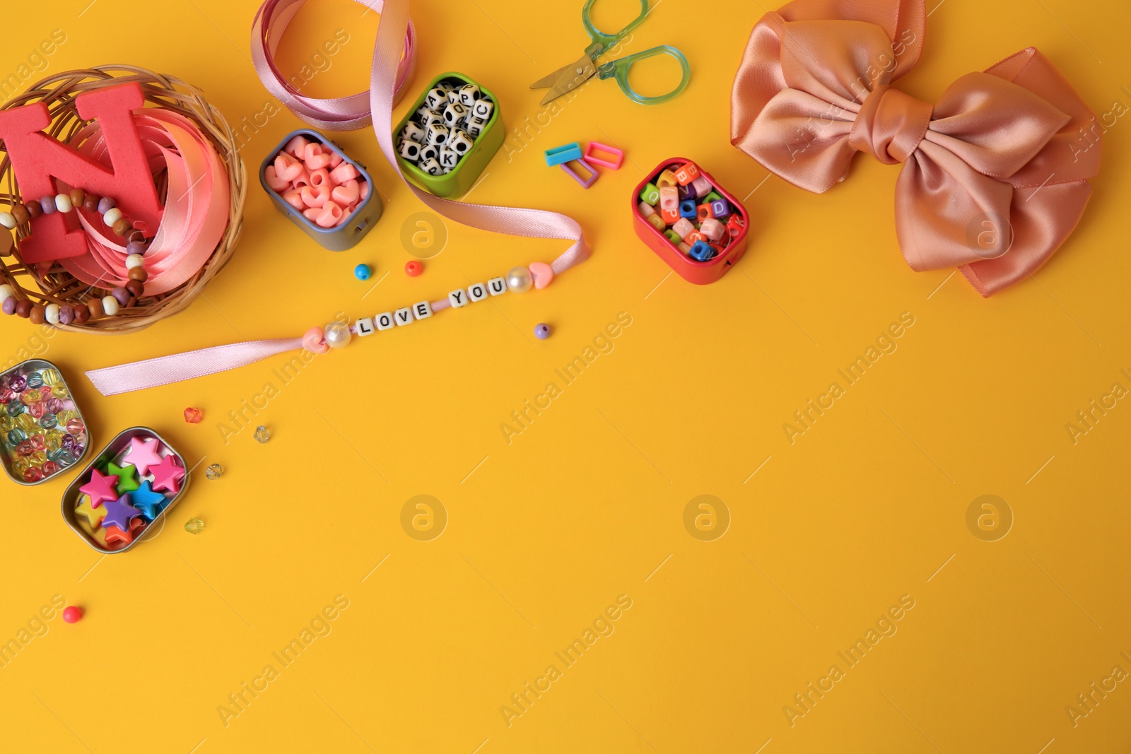 Photo of Kid`s handmade jewelry kit. Colorful beads, ribbon, bow and different supplies on orange background, flat lay. Space for text