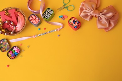 Kid`s handmade jewelry kit. Colorful beads, ribbon, bow and different supplies on orange background, flat lay. Space for text