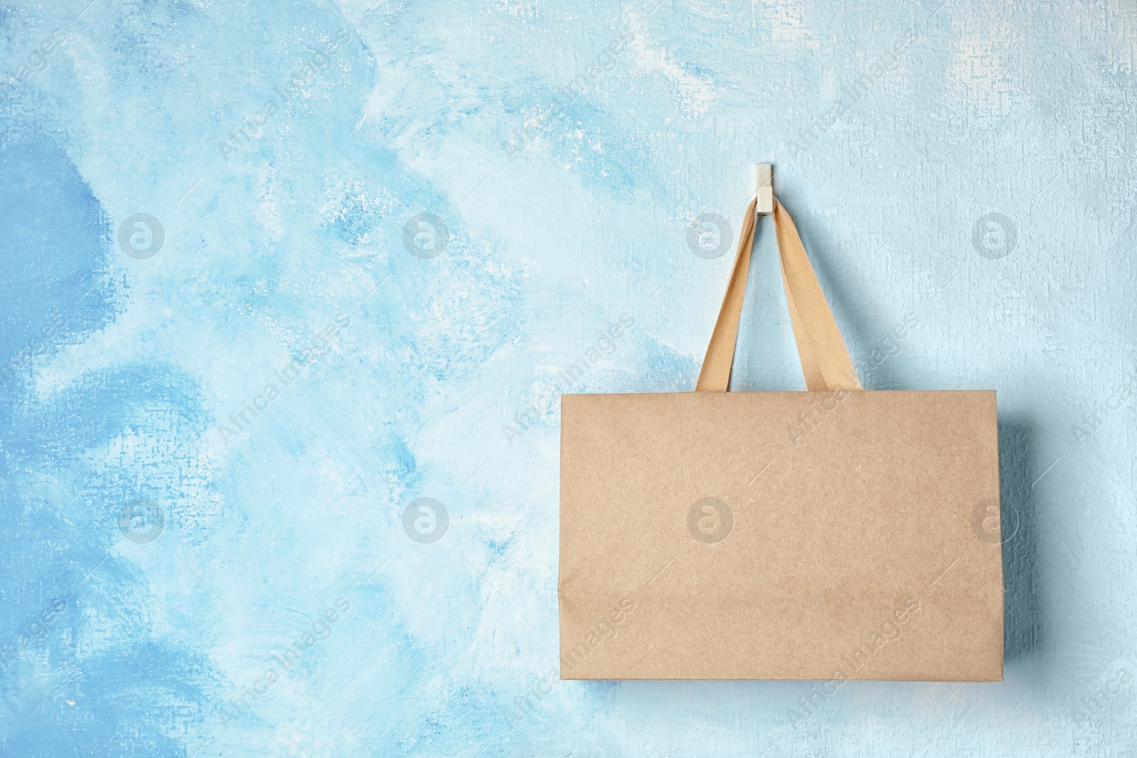 Photo of Paper shopping bag with handles hanging on color wall. Mock up for design