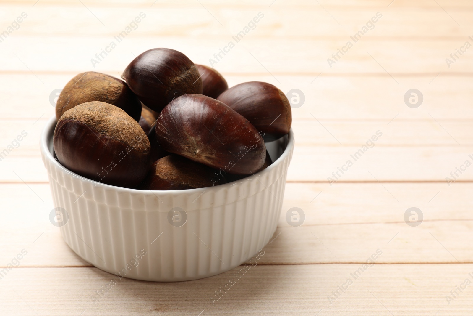 Photo of Sweet fresh edible chestnuts on light wooden table, closeup. Space for text