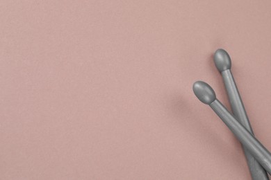 Two gray drum sticks on dusty rose background, top view. Space for text