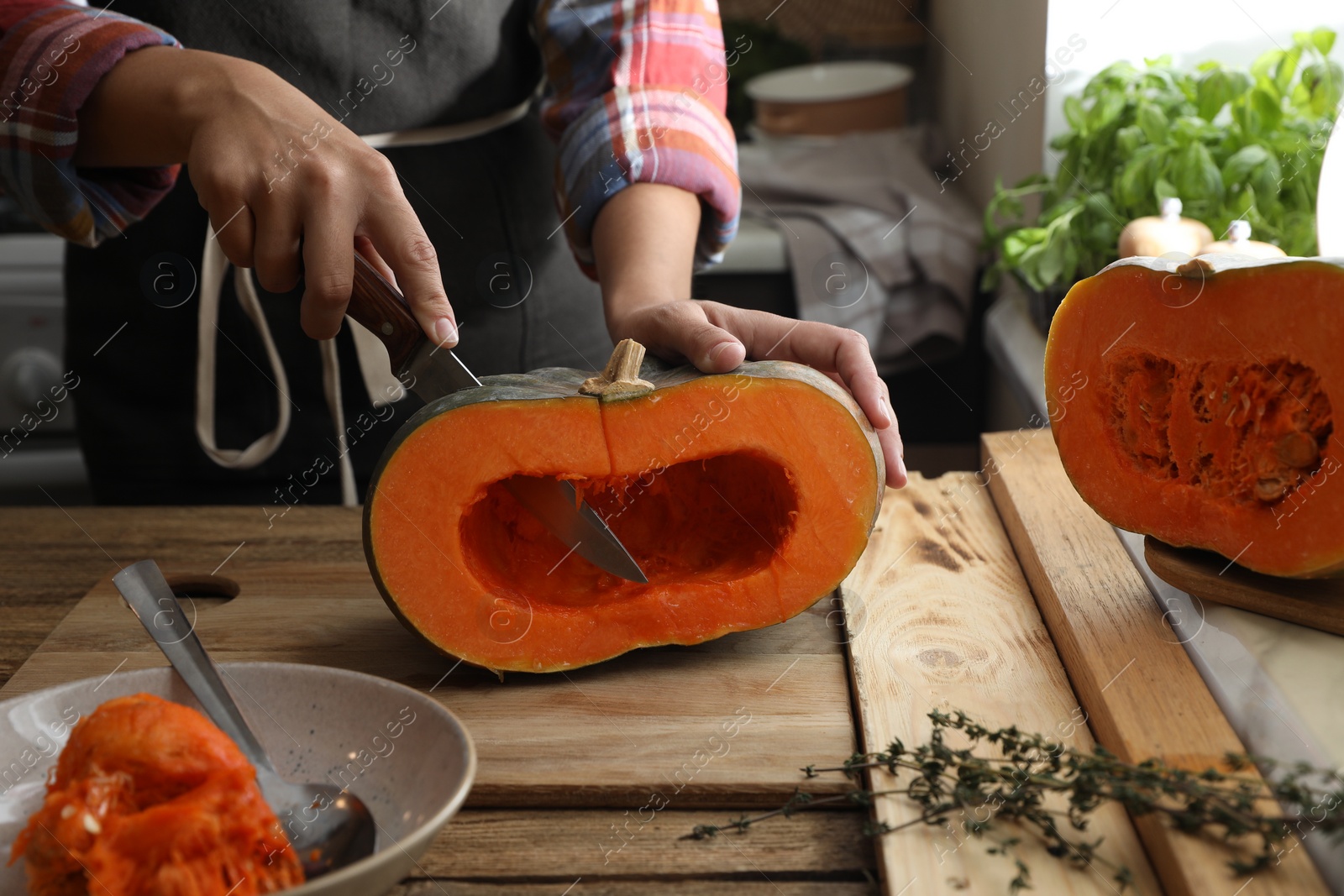 Photo of Woman cutting fresh ripe pumpkin at wooden table in kitchen, closeup