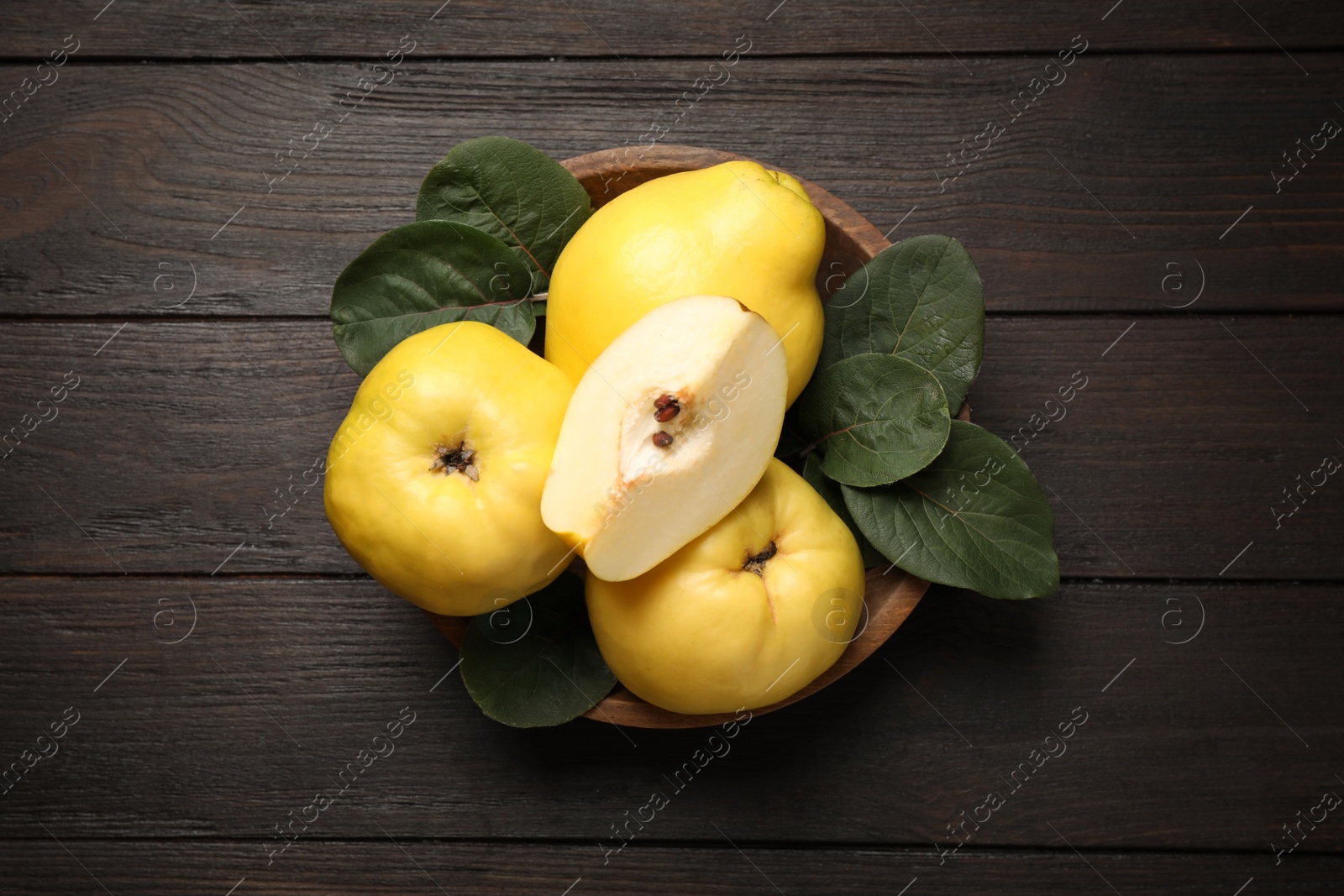 Photo of Fresh ripe organic quinces with leaves on wooden table, top view