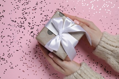 Photo of Christmas present. Woman holding gift box and confetti on pink background, top view