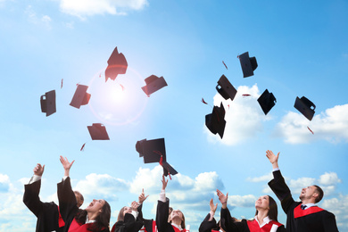 Image of Happy students throwing graduation hats in air outdoors