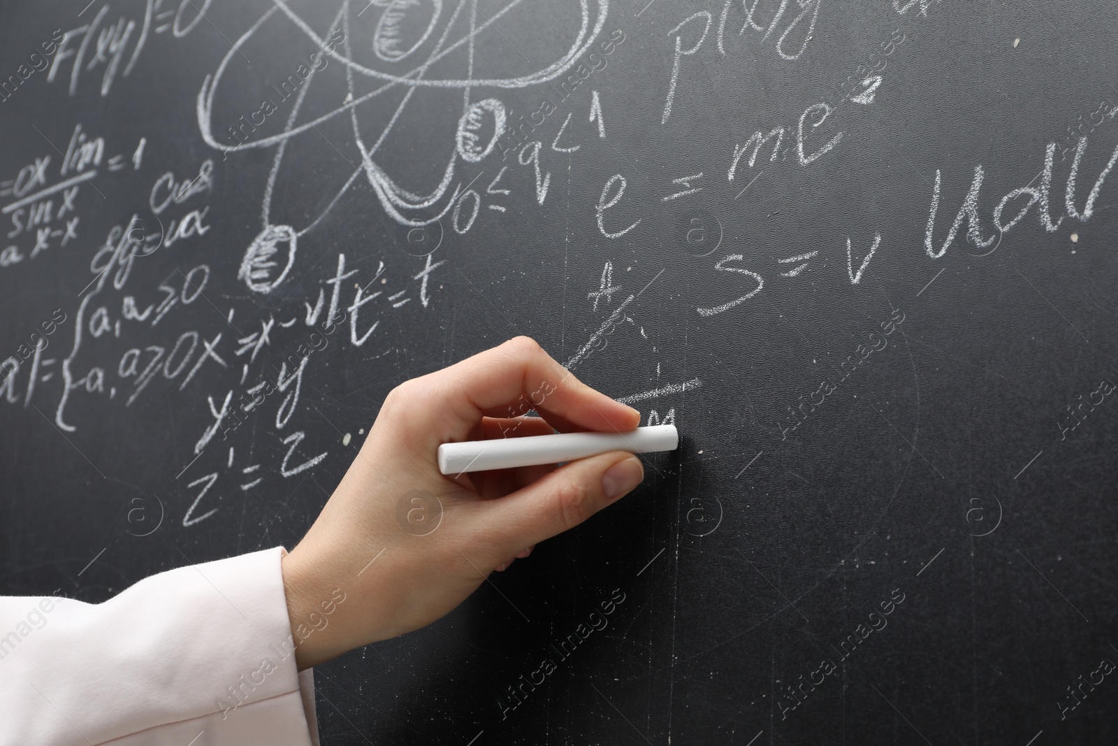 Photo of Teacher writing physical formulas with chalk on black chalkboard, closeup