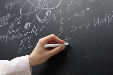 Photo of Teacher writing physical formulas with chalk on black chalkboard, closeup