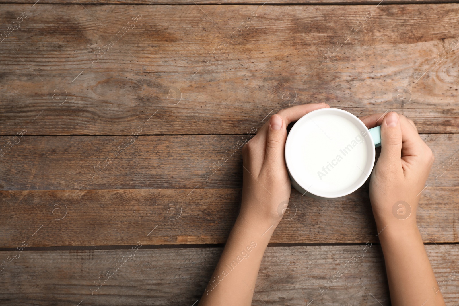 Photo of Woman holding cup of milk on wooden table, top view. Space for text