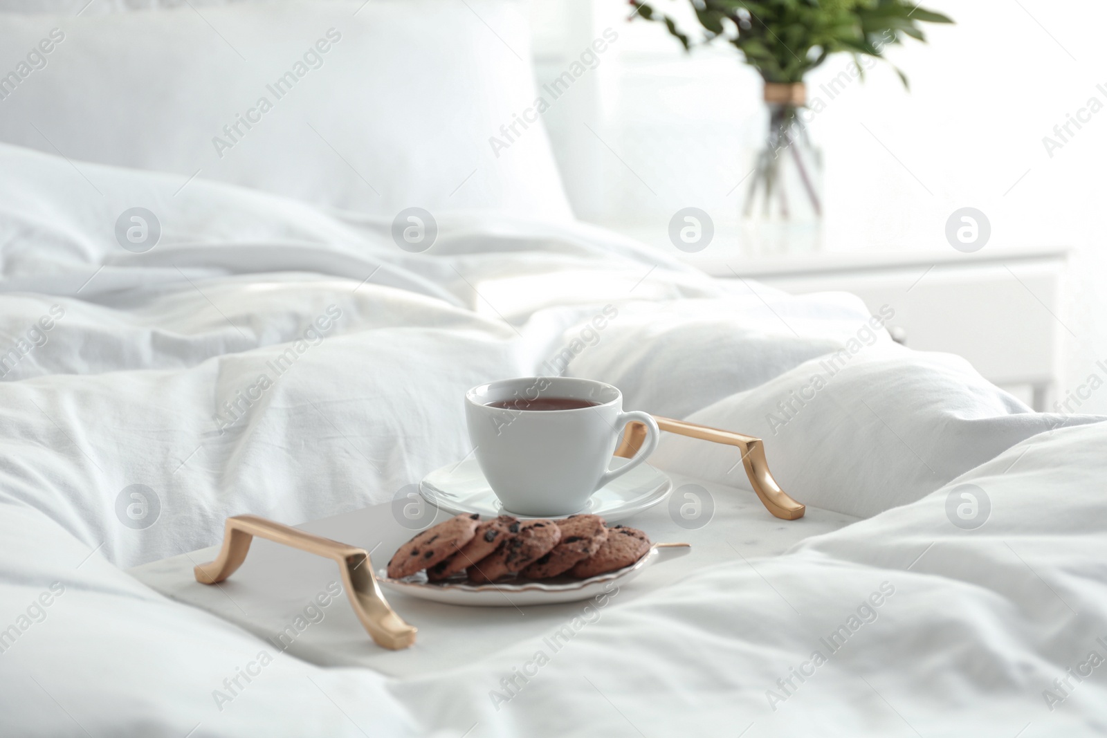 Photo of Cup of aromatic tea and cookies on soft blanket in bedroom