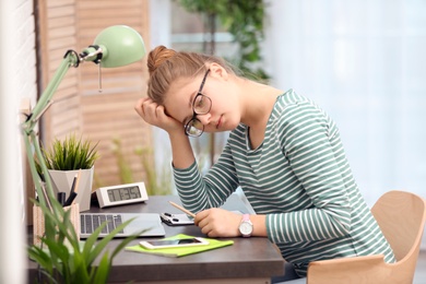 Photo of Upset teenage girl sitting at table in room