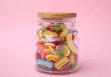 Photo of Tasty colorful candies in glass jar on pink background