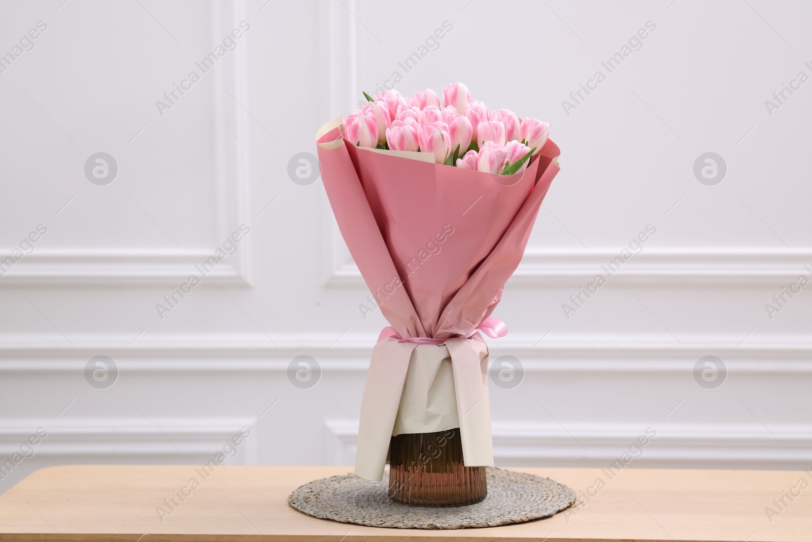 Photo of Beautiful bouquet of fresh pink tulips on wooden table near white wall