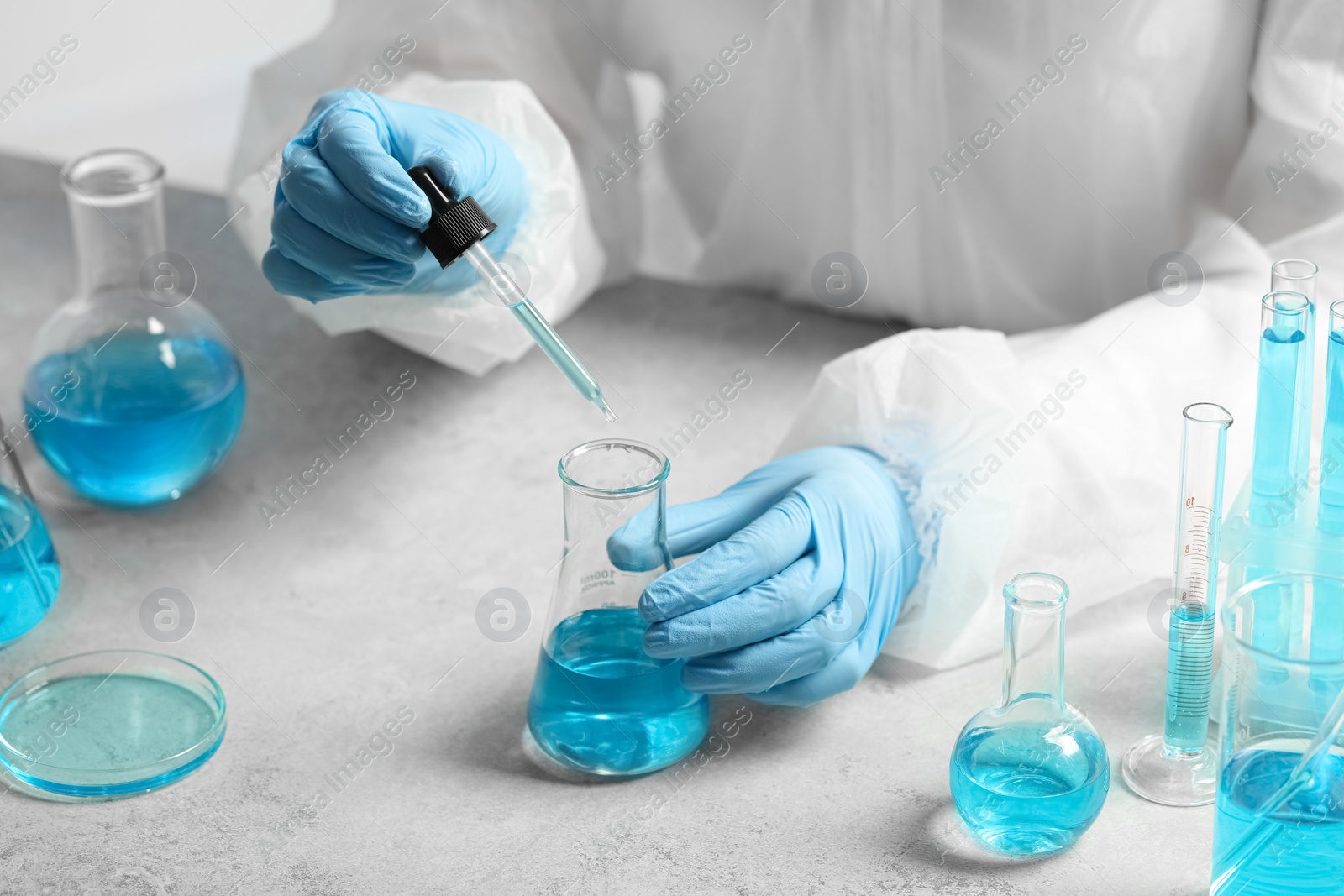 Photo of Scientist dripping liquid from pipette into beaker at white table, closeup