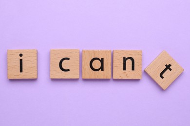 Photo of Motivation concept. Changing phrase from I Can't into I Can by removing wooden square with letter T on violet background, top view