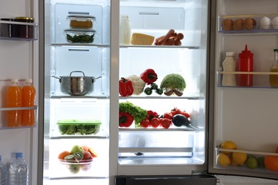 Open refrigerator full of different products in kitchen