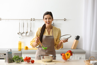 Young woman cooking tasty soup in kitchen