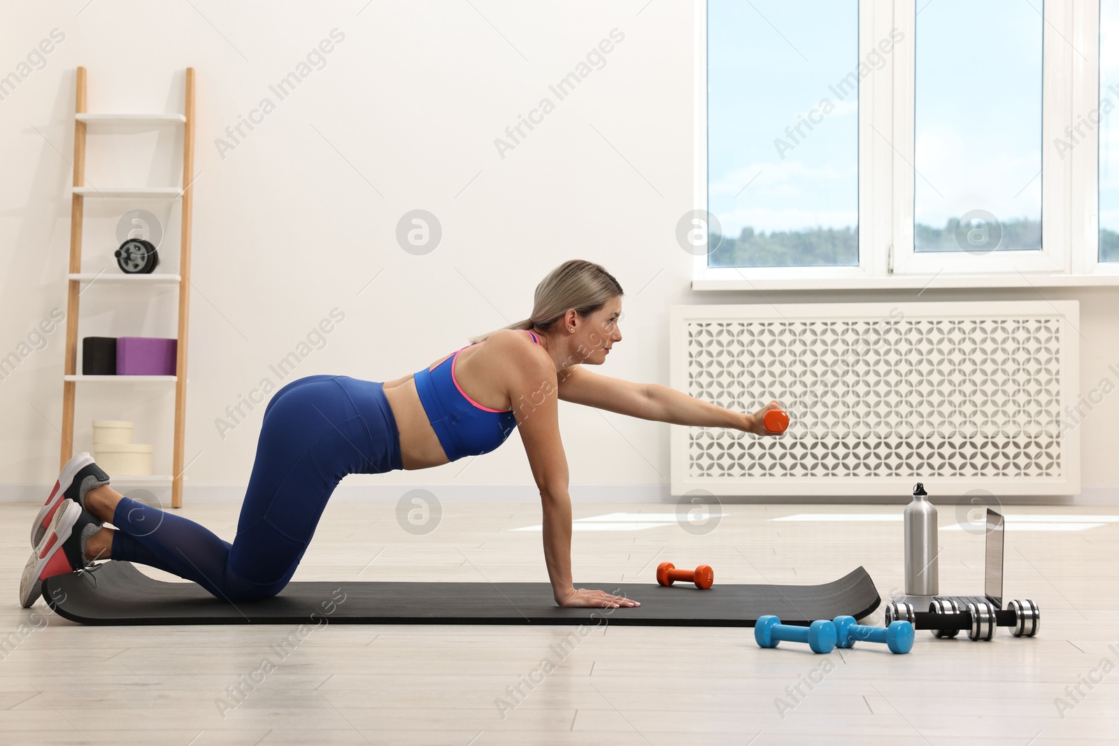 Photo of Online fitness trainer. Woman doing exercise with dumbbells near laptop at home