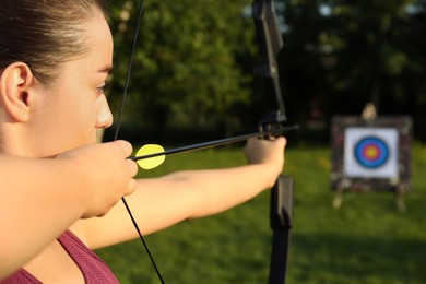 Photo of Woman with bow and arrow aiming at archery target in park, closeup