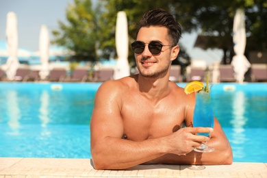 Photo of Young man with cocktail in pool on sunny day
