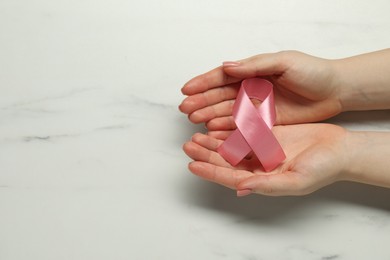 Photo of Breast cancer awareness. Woman with pink ribbon at white marble table, top view. Space for text