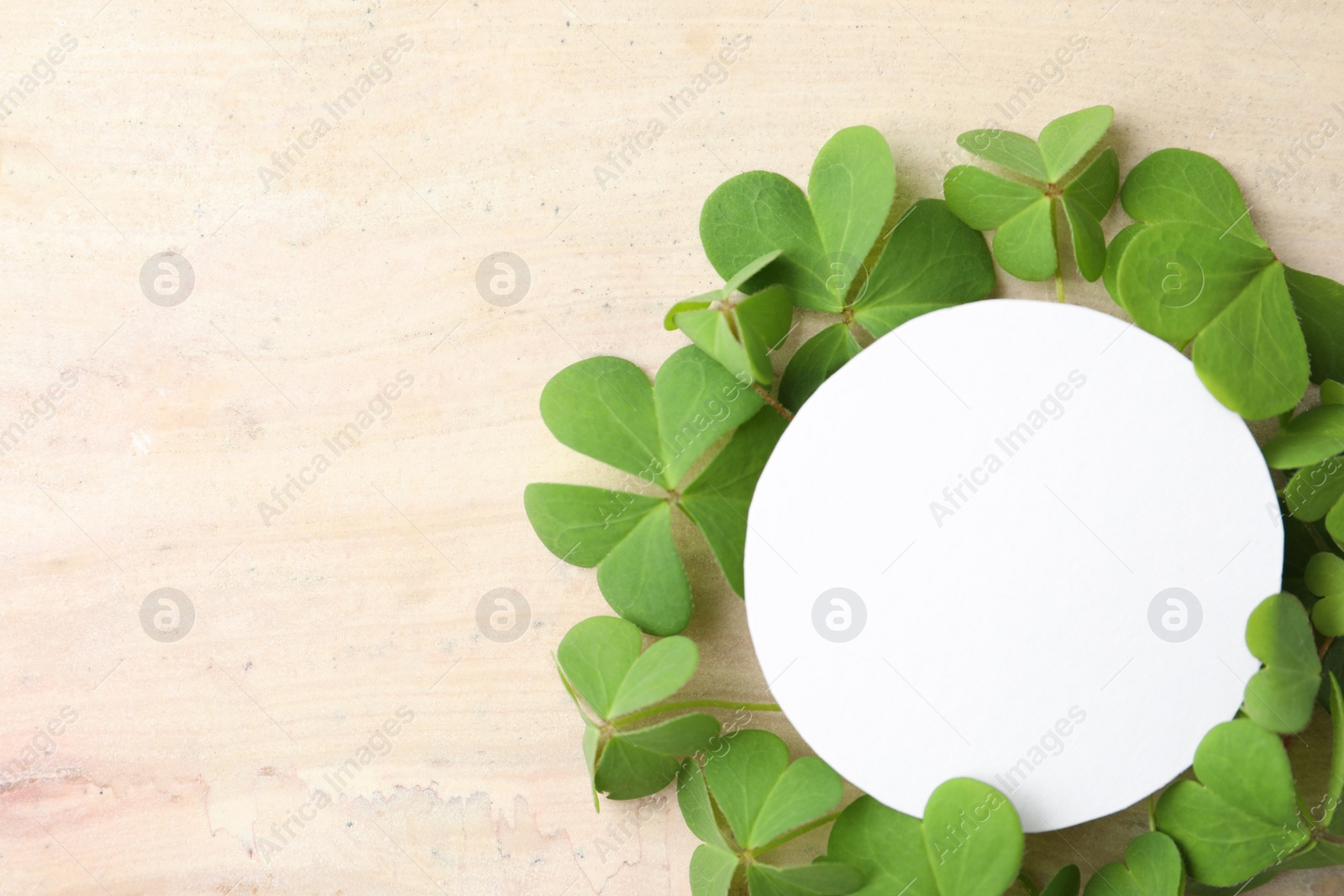 Photo of Frame of clover leaves and blank card on light table, flat lay with space for text. St. Patrick's Day celebration