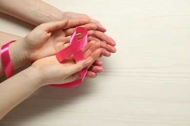 Photo of Breast cancer awareness. Women holding pink ribbon at white wooden table, top view. Space for text