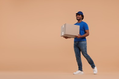Happy young courier with parcel on light brown background, space for text