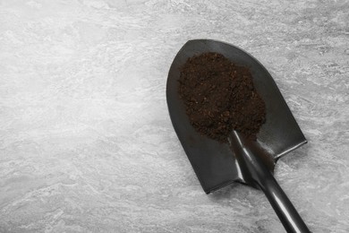 Photo of Metal shovel with fertile soil on grey textured surface, top view. Space for text