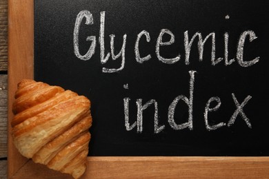 Small chalkboard with words Glycemic Index and croissant on table, top view