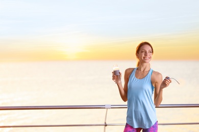 Photo of Young woman holding bottle with water on pier. Morning workout