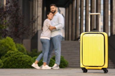 Photo of Long-distance relationship. Young couple hugging near building outdoors, focus on yellow suitcase