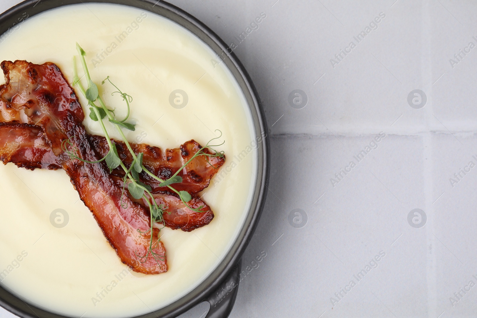 Photo of Delicious potato soup with bacon and microgreens in bowl on white tiled table, top view. Space for text