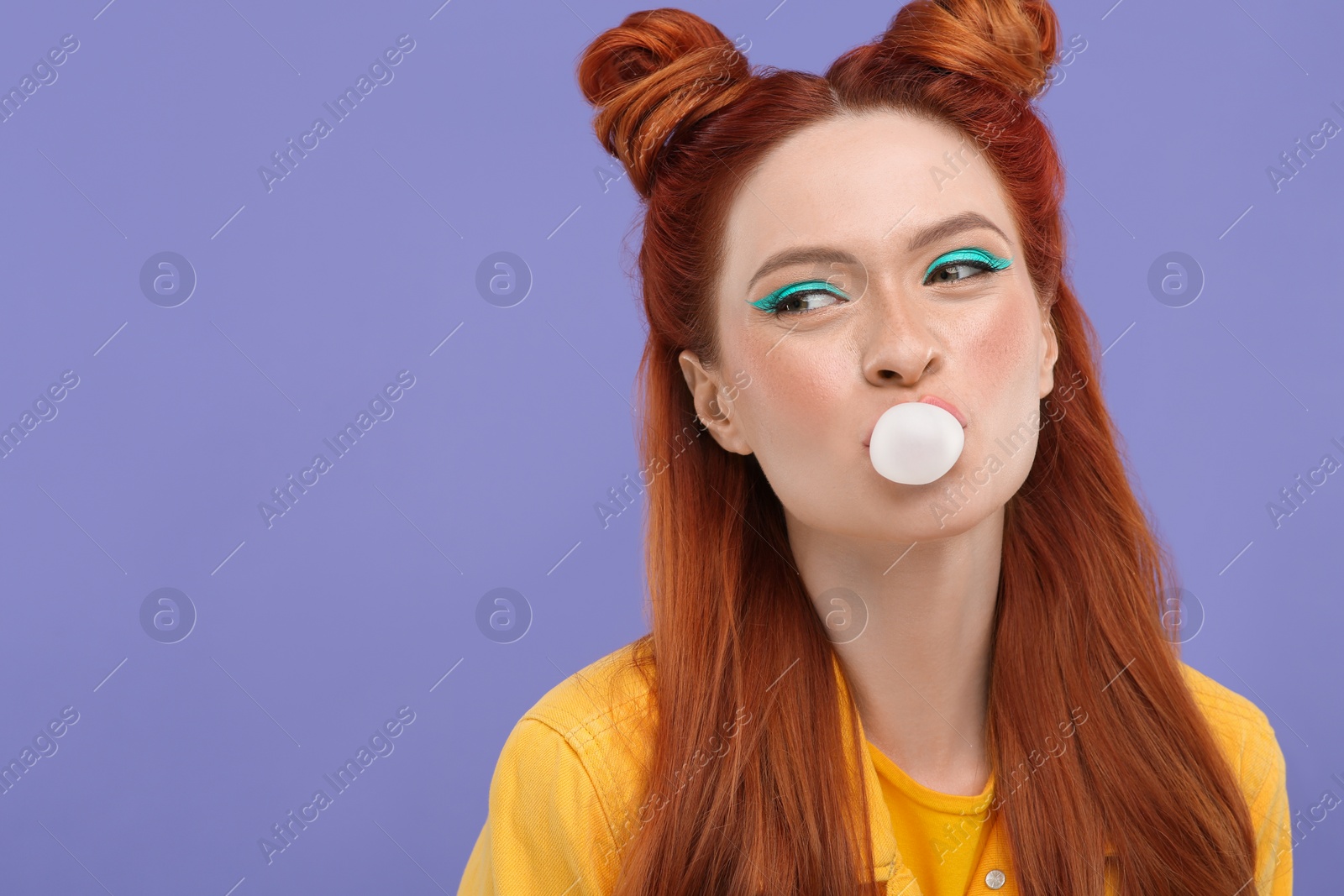 Photo of Portrait of beautiful woman with bright makeup blowing bubble gum on violet background. Space for text