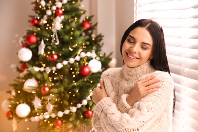 Photo of Young woman near window in room with Christmas tree, space for text