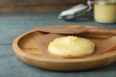 Photo of Plate and knife with Ghee butter on light blue wooden table, closeup.