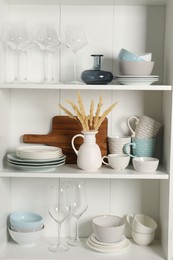 Photo of Different clean dishware and glasses on shelves in cabinet indoors