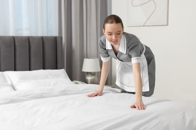 Young maid making bed in hotel room. Space for text