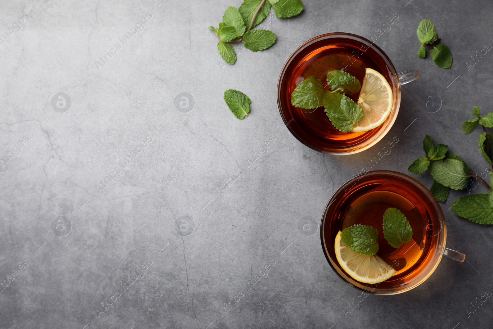 Photo of Cups of aromatic herbal tea with mint and lemon on grey table, flat lay. Space for text