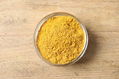 Curry powder in bowl on wooden table, top view